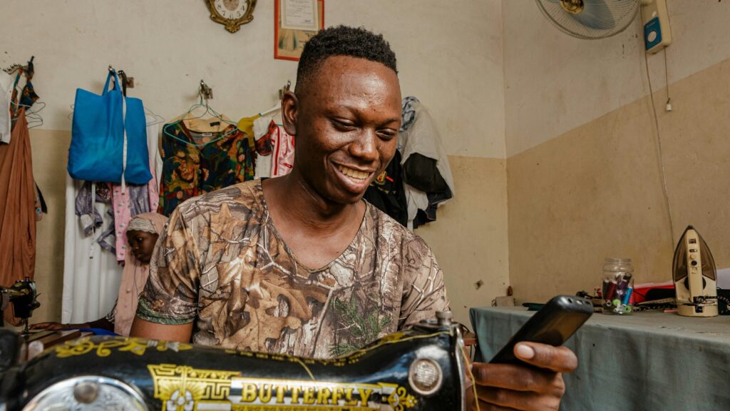 Tailleur souriant consultant son téléphone près de sa machine à coudre